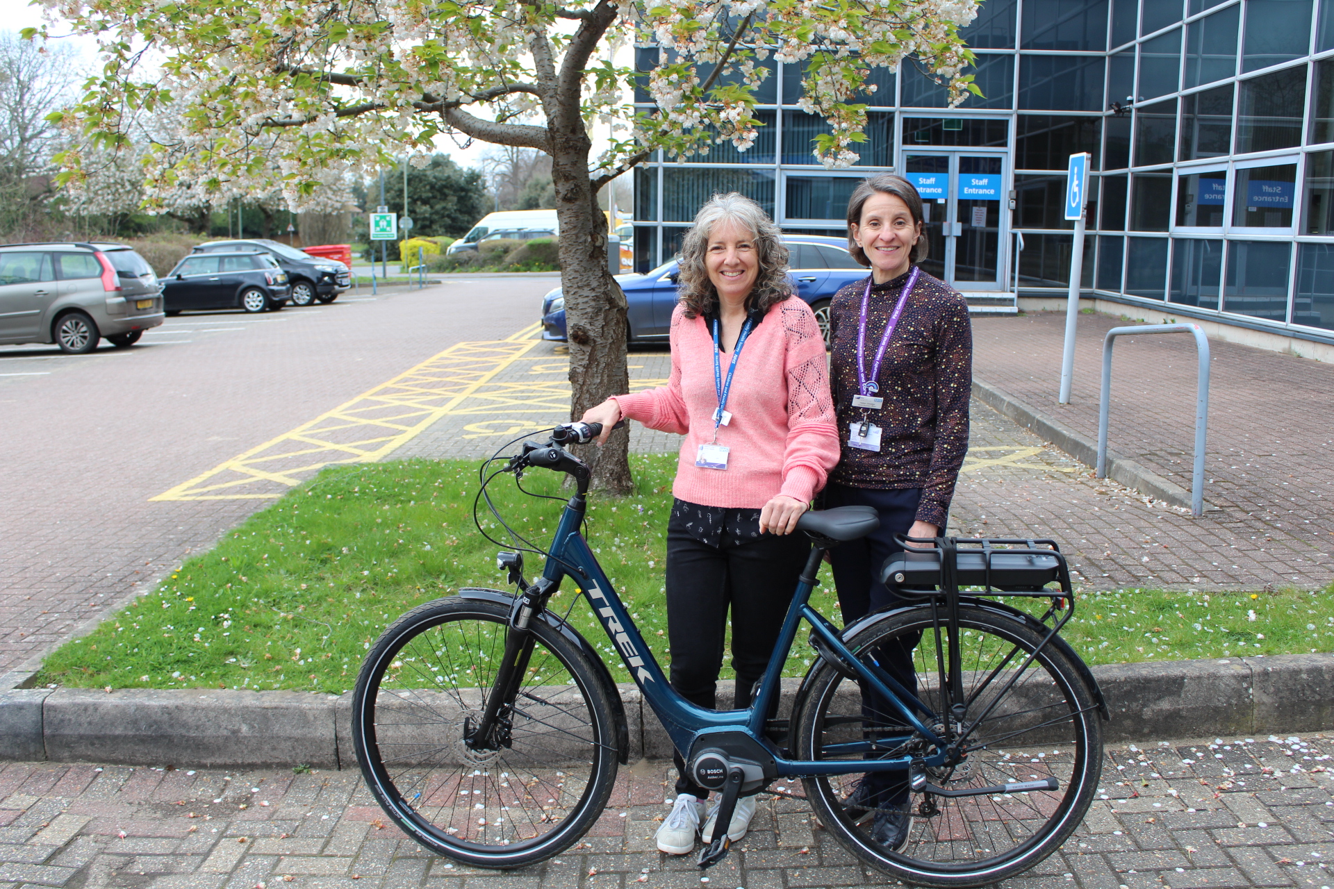 Chris Jones and Helen Dredge stood in front of a tree in a car park with a blue electric bike